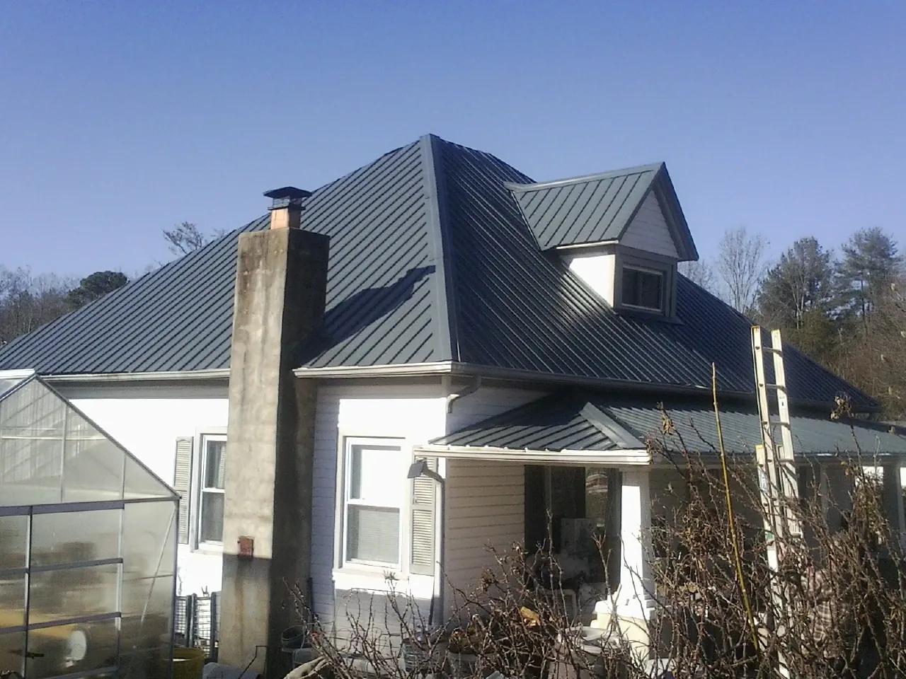 Dark blue standing seam metal roof on a white farmhouse with dormer — Slate & Tile Roof Repair by Roofing Brothers in Billings