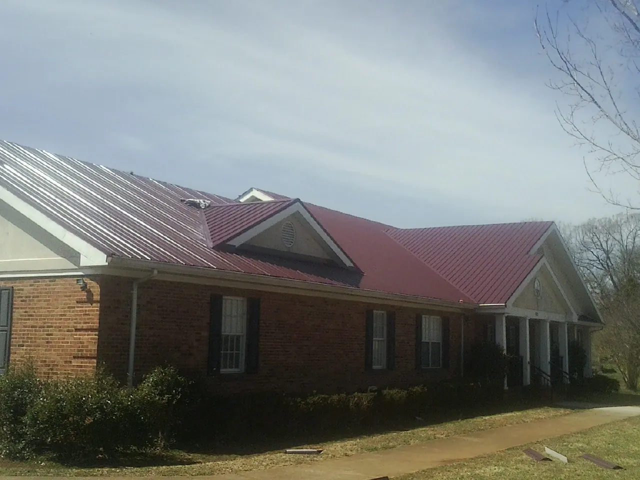 Red metal roof with gabled entries on a long brick building, from a Hail Damage Roof Repair job in Billings
