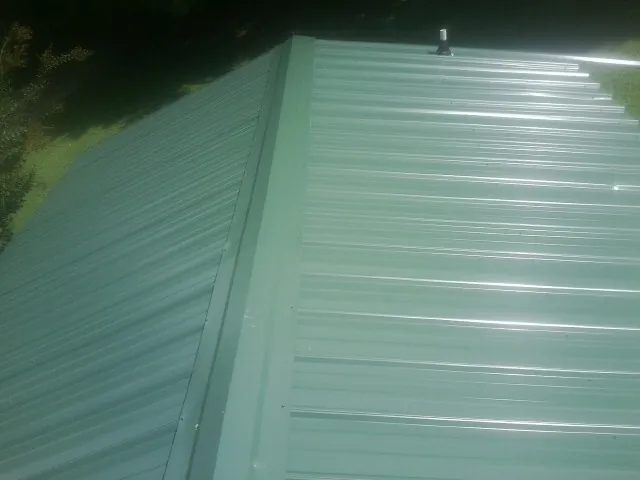 New green metal panels meeting at the ridge of a roof — Flat Roof Repair work by our crew in Billings