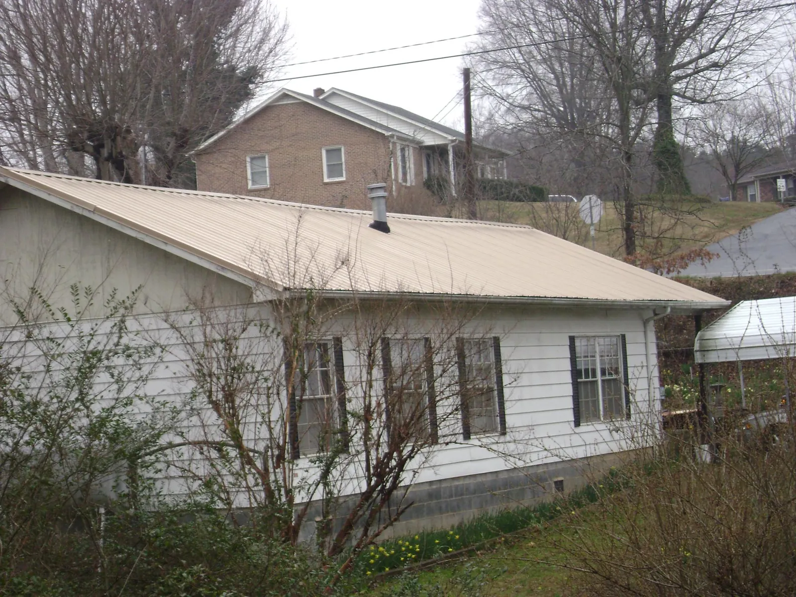 Tan metal roof on a white sided house set into a hillside — Commercial Roofing by Roofing Brothers in Billings